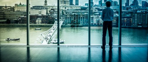 Businessman looks at the London Skyline from his Office Window