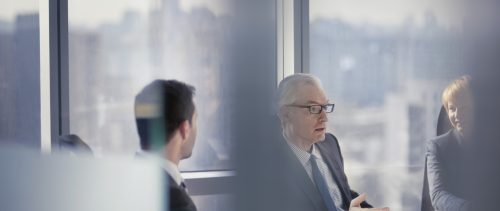 Through the glass view of businessman talking to colleagues in conference room meeting