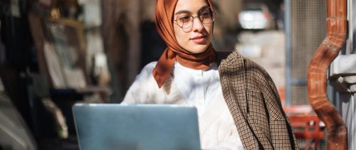 Young woman sitting at sidewalk cafe and using Laptop